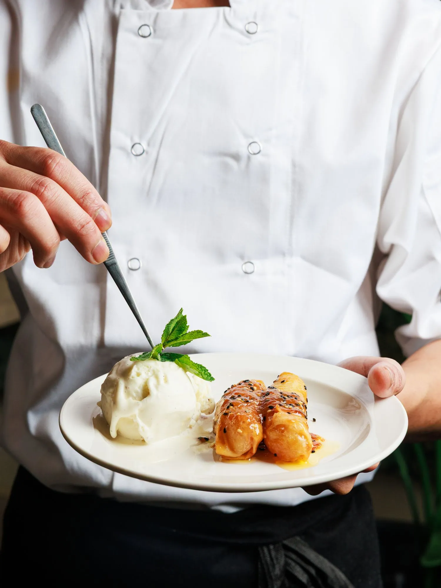 Chef finishing a dessert plate with ice cream and glazed rolls at Mina's Table.