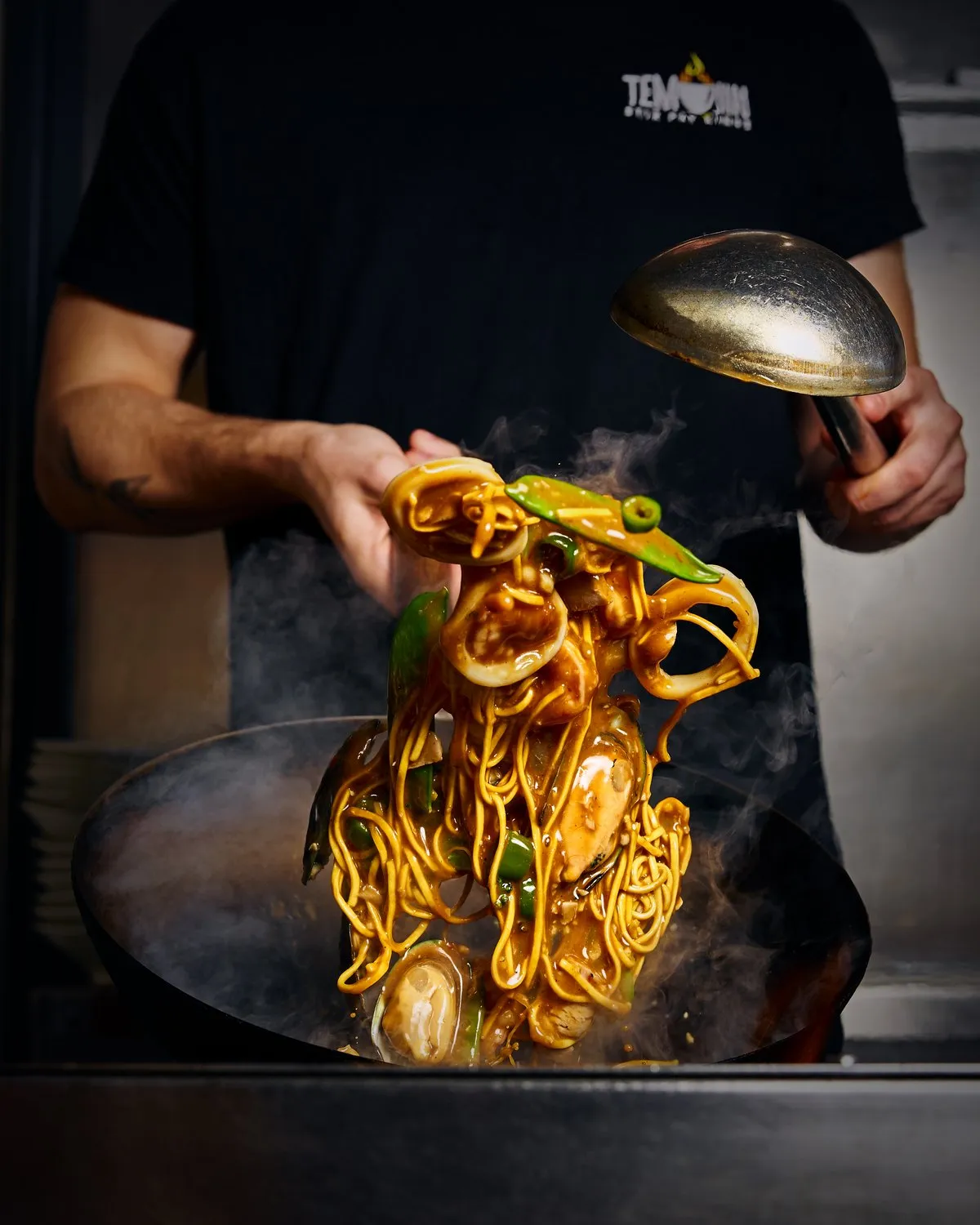 Chef tossing noodles, mussels and peppers in a steaming wok at Temujin.